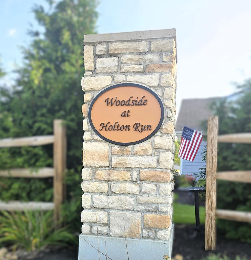 Woodside at Holton Run sign on a stone column beside a split rail fence