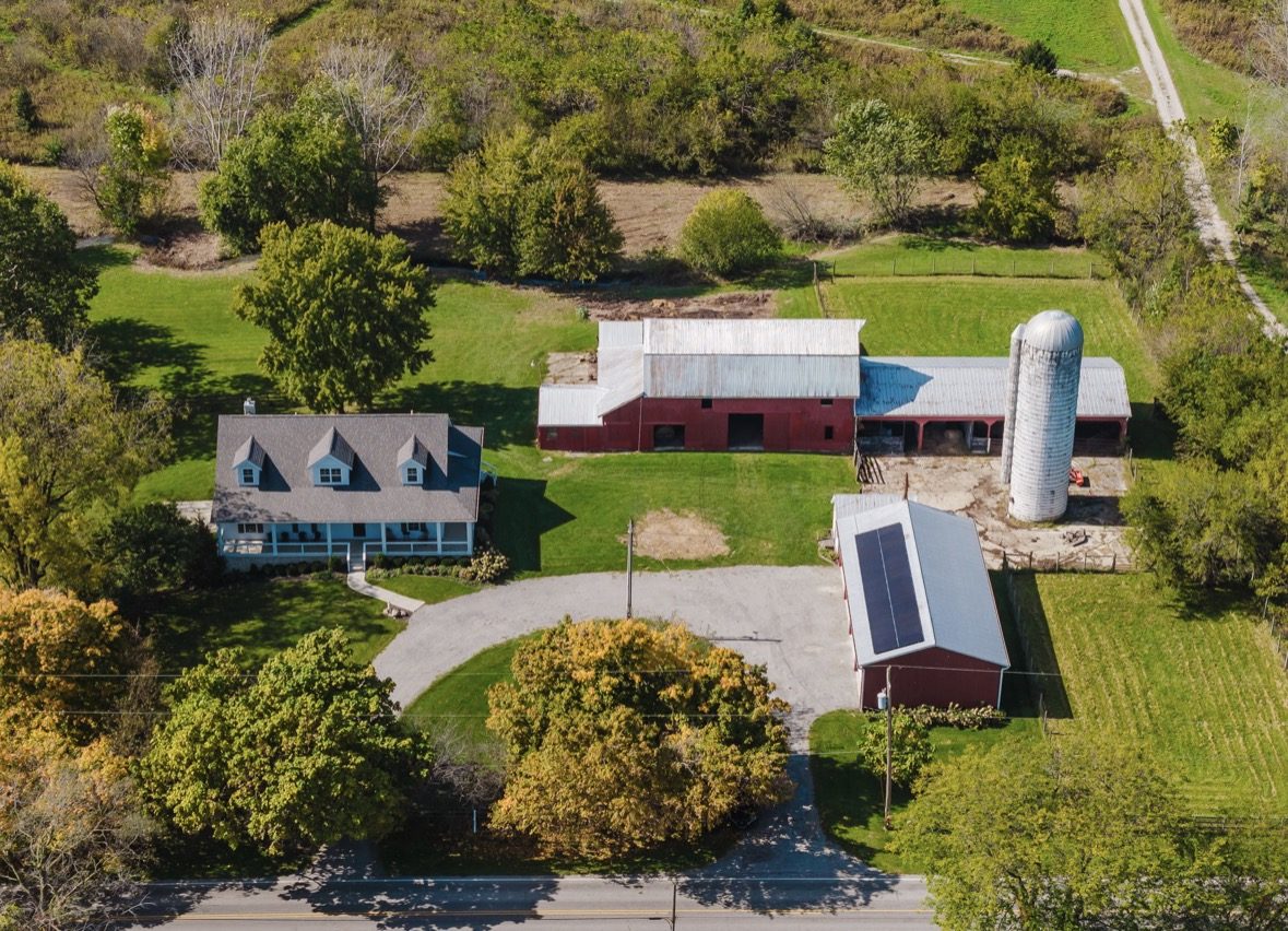 Aerial view of 14875 State Rd: the farmhouse, the red barn and silo, and a second outbuilding with solar panels around a circle drive